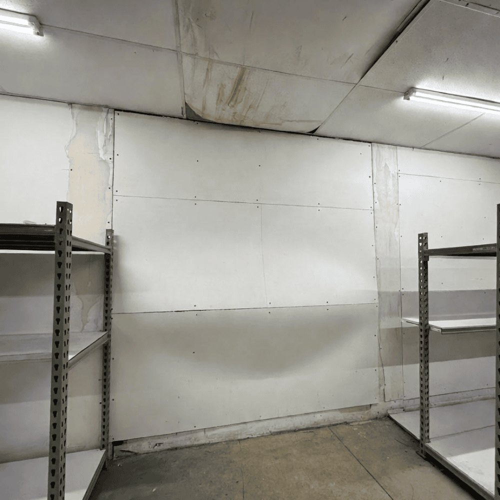 Bowed interior drywall wall with water-stained ceiling panels in a storage room