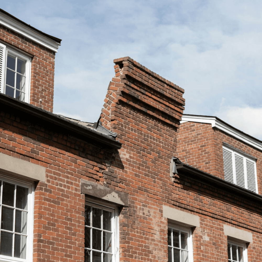 Leaning brick parapet with displaced courses and deteriorated mortar above a building roofline