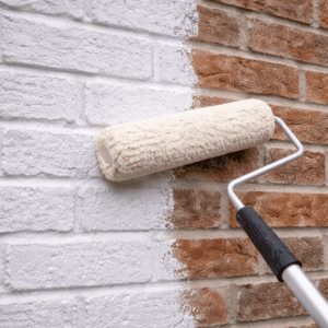 Paint roller applying white coating across a red brick wall
