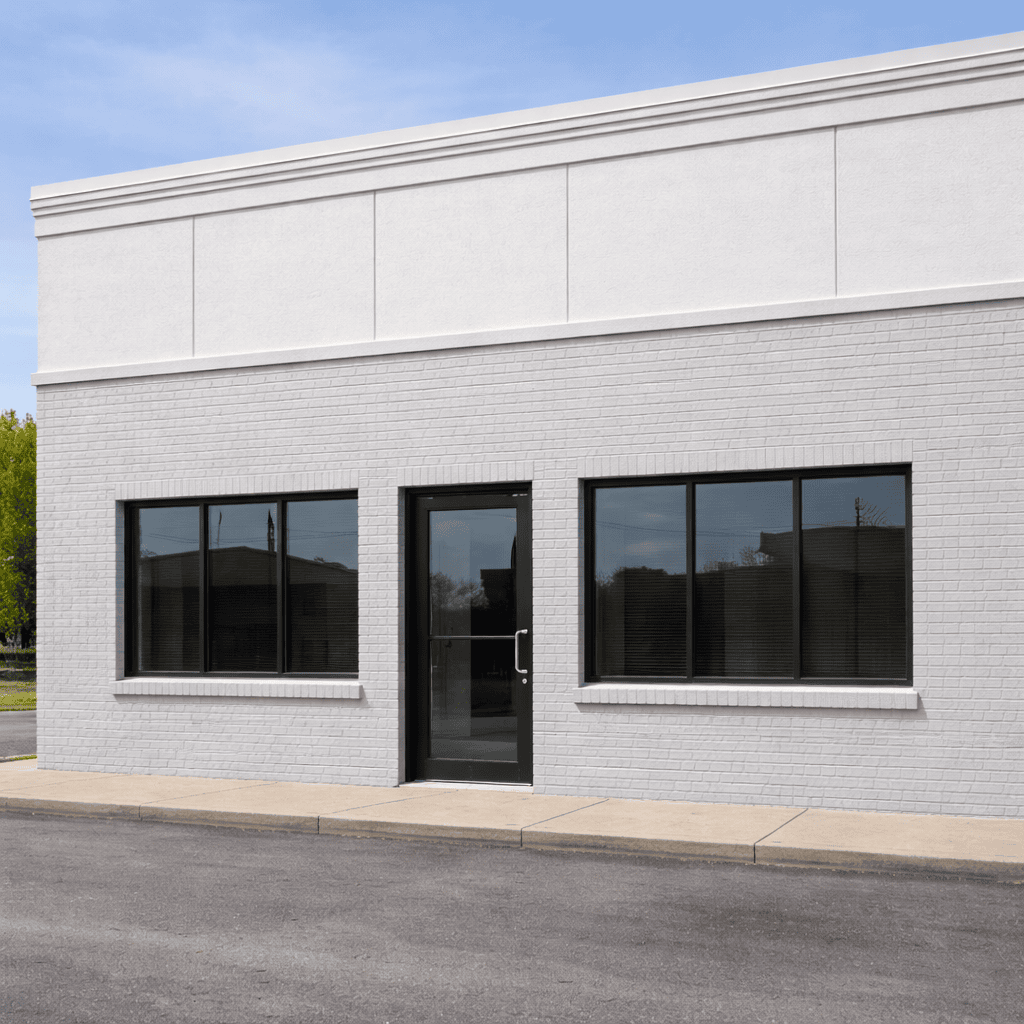 White-coated commercial brick facade with black-framed windows and a glass entrance door