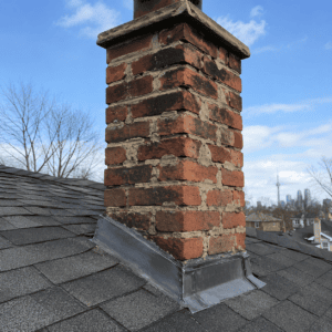 Weathered brick chimney with deteriorated mortar and flashing near the roofline