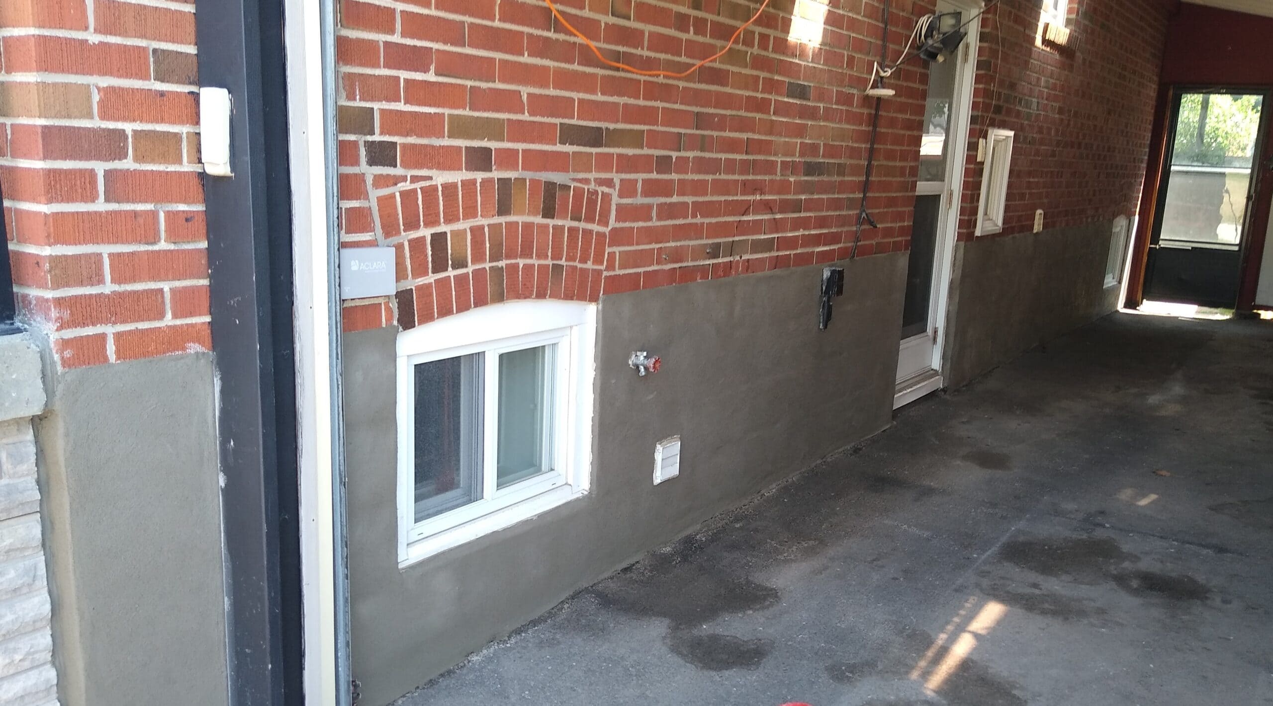 Red brick wall with gray parging around a basement window and exterior doorway