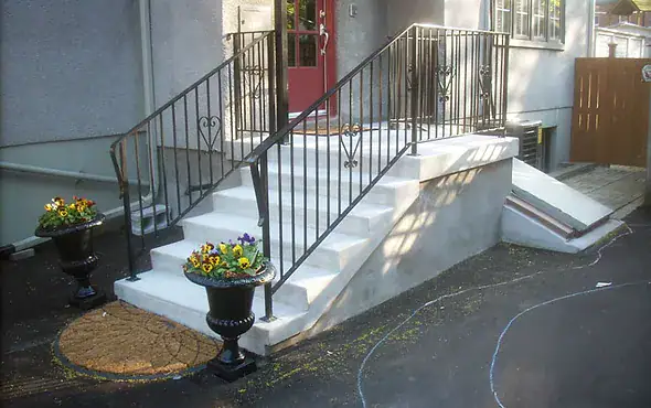 White concrete front steps with black metal railings leading to a red entry door