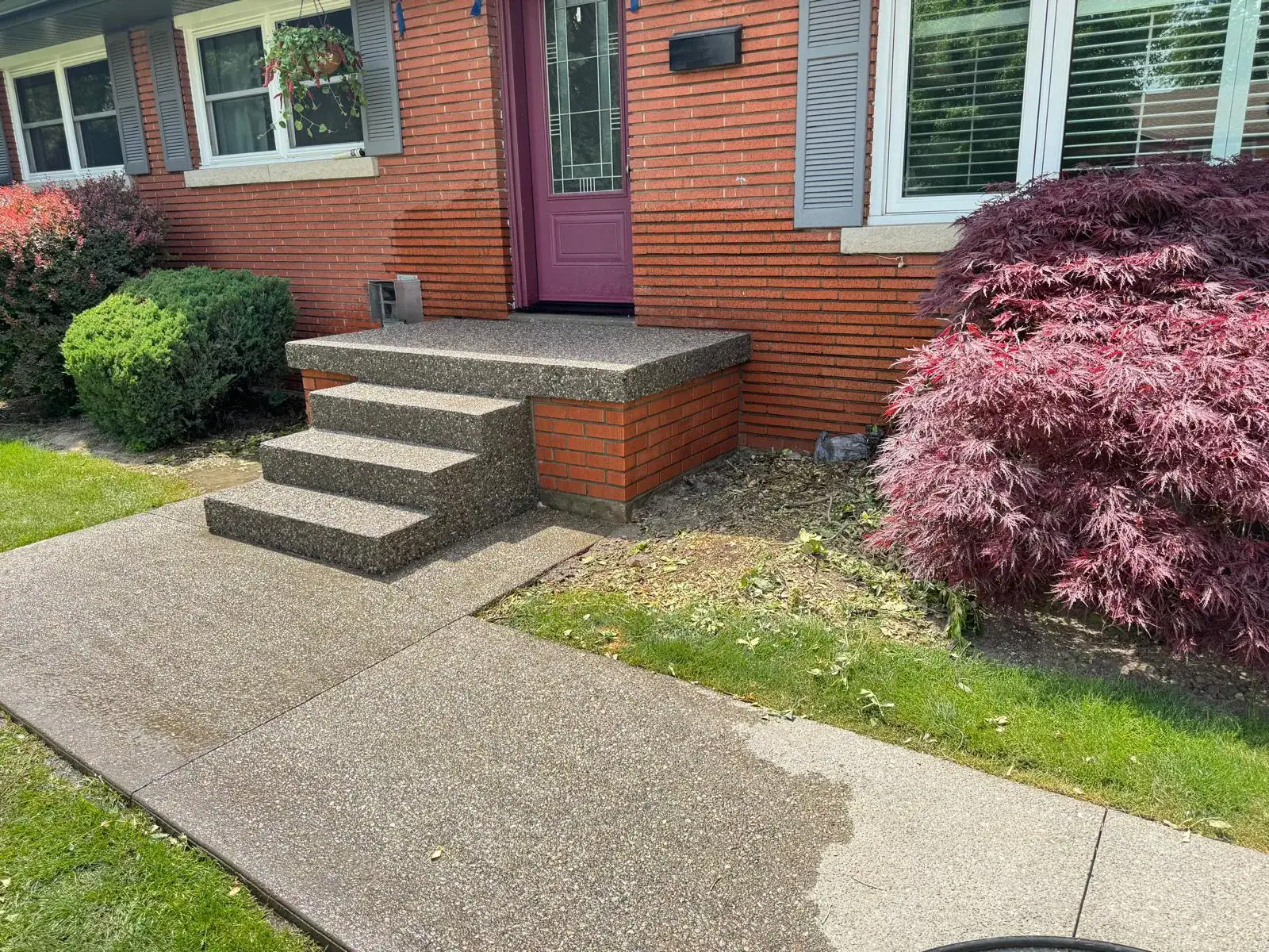 Concrete steps and walkway in front of a brick house with purple door.