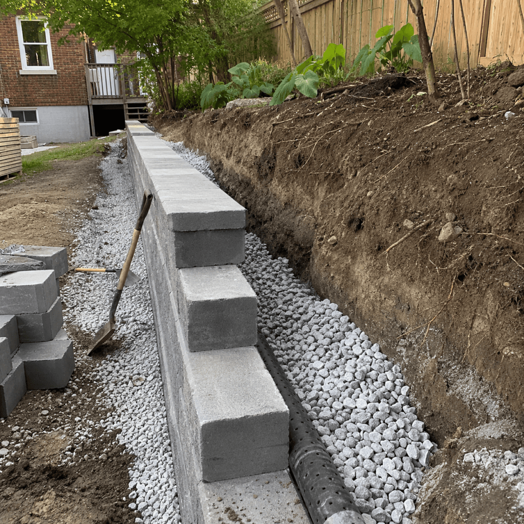 Retaining wall drainage stone and pipe behind a wall under construction