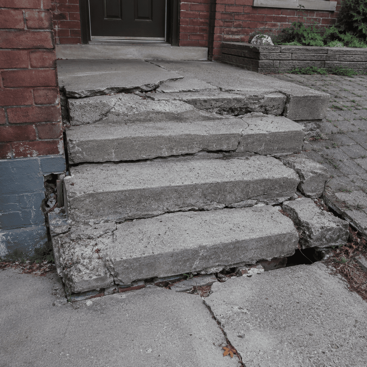 Damaged concrete entrance steps with deep cracks, spalling edges, and uneven treads