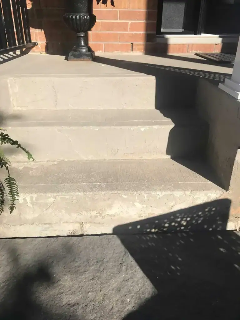 Worn concrete front porch steps and landing with visible surface cracks and weathering