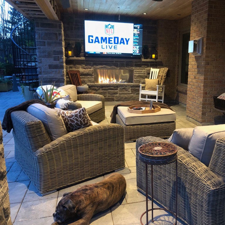 Cozy outdoor seating area with fireplace and TV for game day entertainment.