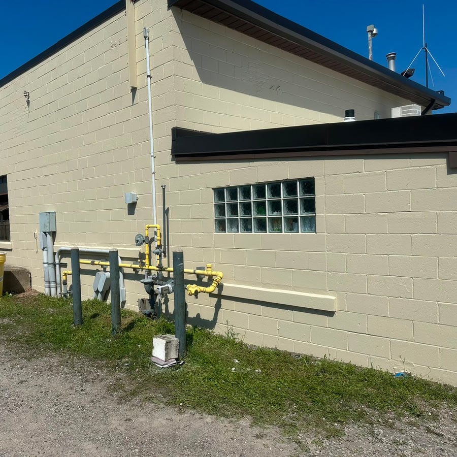 Exterior view of a masonry wall with glass block window and utility pipes.