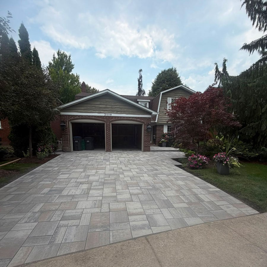 Modern masonry driveway leading to a suburban house with lush landscaping.