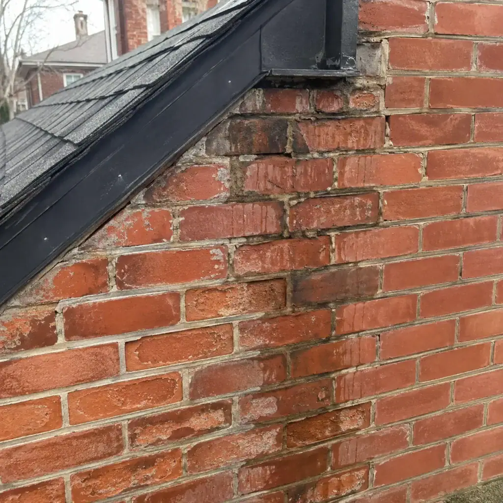 Cracked and deteriorating brick masonry at roof-wall junction.