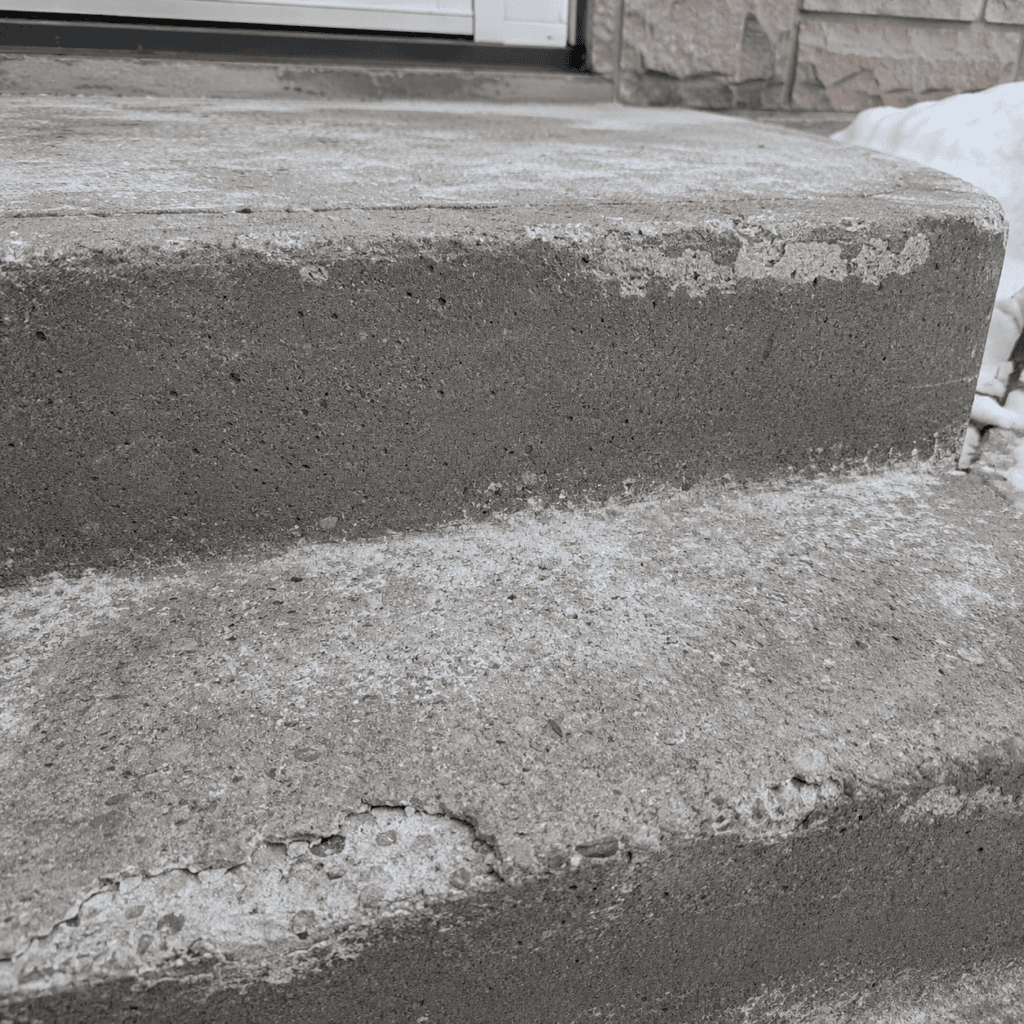 Weathered concrete steps with surface spalling and exposed aggregate beside winter snow