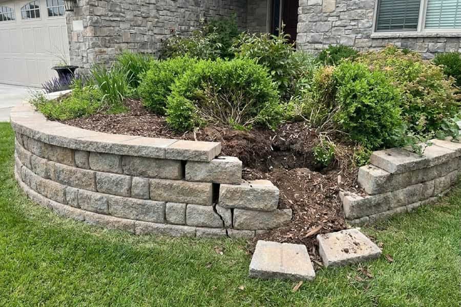 Partially collapsed garden retaining wall with displaced concrete blocks beside a raised planting bed