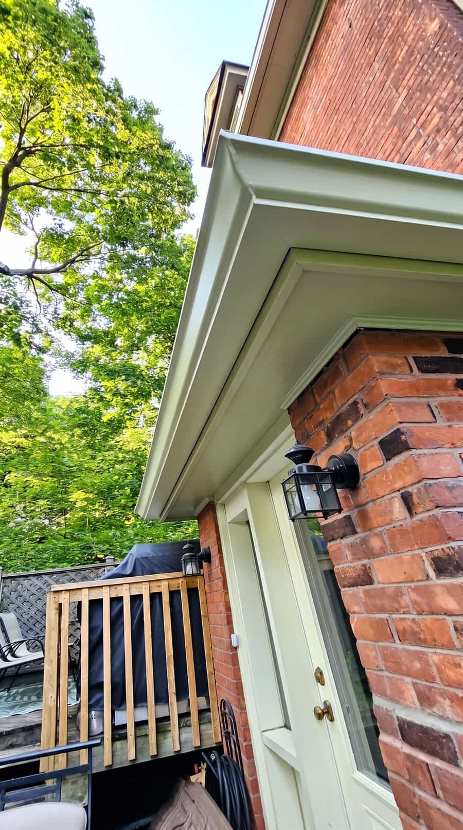 White eavestrough running along a brick house roofline above the soffit and exterior door