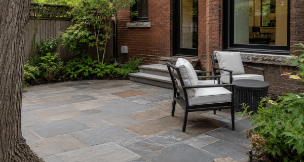 Natural stone patio beside a brick home with stone steps, garden beds, and outdoor seating
