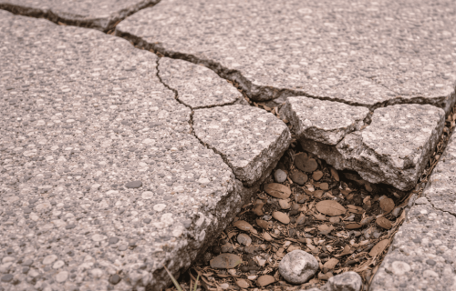 Cracked, uneven exposed-aggregate concrete slabs with a wide gap filled by leaves and gravel