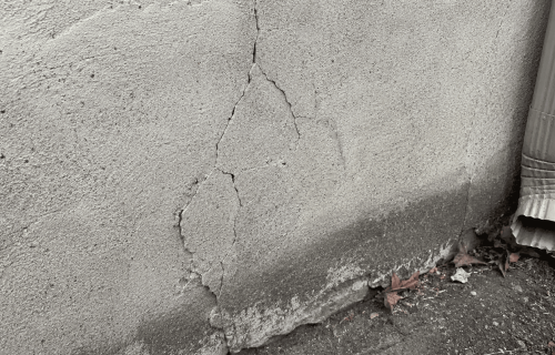 Cracked parging on a foundation wall with deteriorated material along the lower edge
