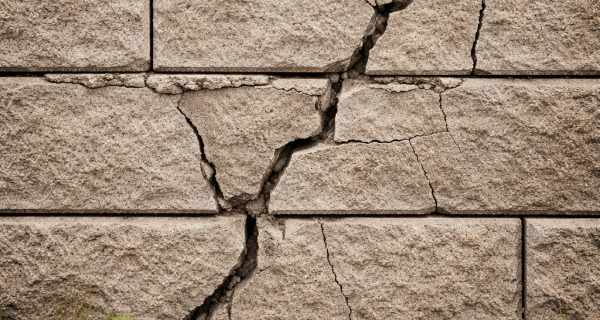 Cracked masonry retaining wall with displaced blocks and fallen debris along its base
