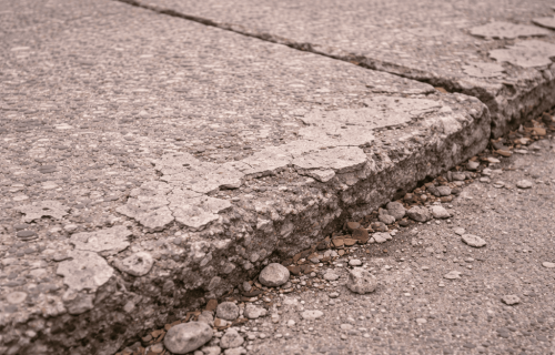 Close-up of spalling concrete walkway with exposed aggregate and broken, uneven edge