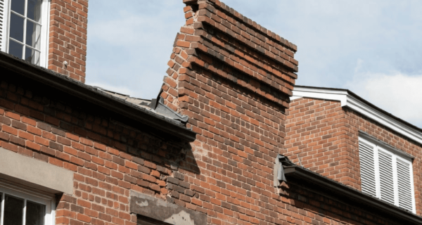 Leaning brick parapet with displaced courses and deteriorated mortar above a building roofline