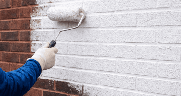 Worker applies a white coating to a red brick wall with a paint roller