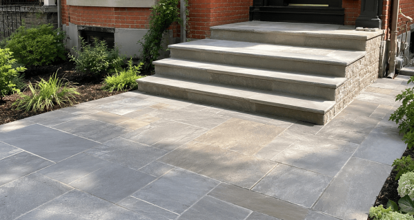 Broad stone steps lead from a paved patio to a black door in a red brick entryway