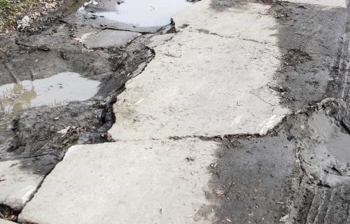 Cracked, uneven concrete driveway with broken slab edges, muddy joints, and standing water