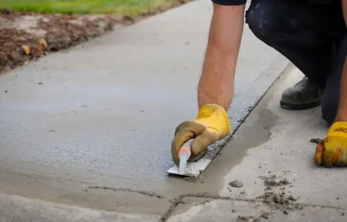 Worker smooths fresh concrete along the edge of a residential walkway
