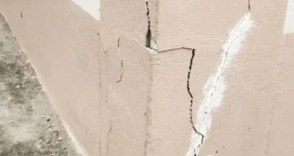 Cracked parging along a foundation wall corner with several vertical cracks and visible patching