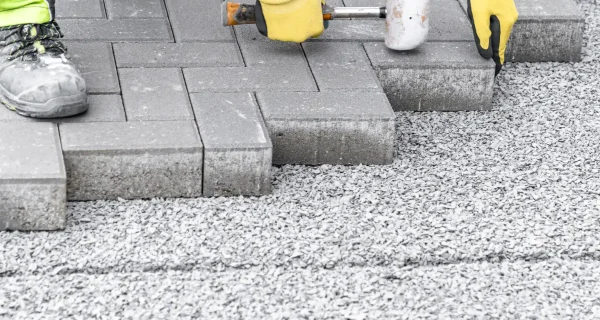 Worker setting gray interlocking pavers with a rubber mallet over a compacted gravel base