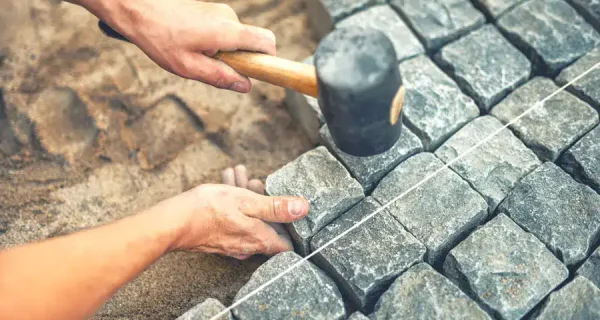 Hands use a rubber mallet to align natural stone pavers along a guide string