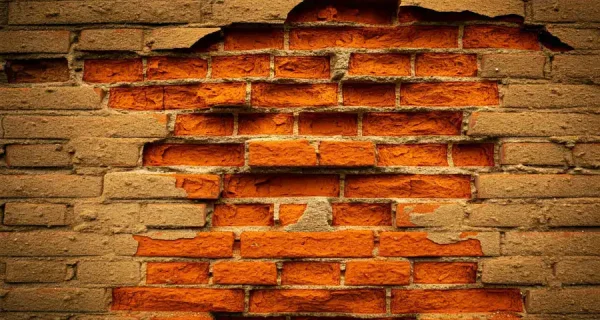 Spalled brick wall exposing deteriorated red bricks beneath the masonry surface
